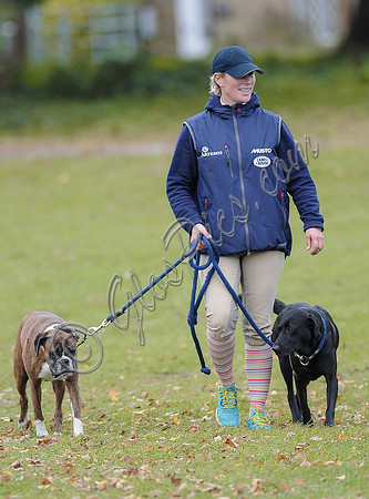 Walking towards camera looking left, Zara Phillips in blue MUSTO jacket and polo cap, with boxer and labrador.