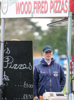 Zara Phillips in blue MUSTO jacket at Pizza stand with "Wood Fired Pizzas" overhead.