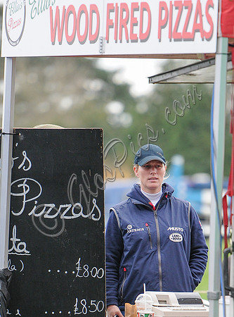 Zara Phillips in blue MUSTO jacket at Pizza stand with "Wood Fired Pizzas" overhead.
