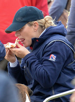 tight side shot of Zara Phillips eating a pizza wearing polo cap and blue MUSTO jacket