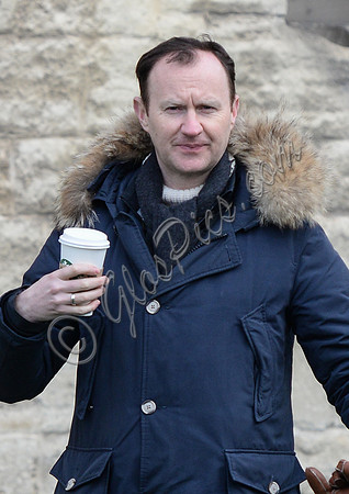 Mark Gatiss wearing blue Parka, carrying large polystyrene cup.