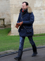 Mark Gatiss wearing fur collared blue Parka coat and leather gloves carrying polystyrene coffee cup