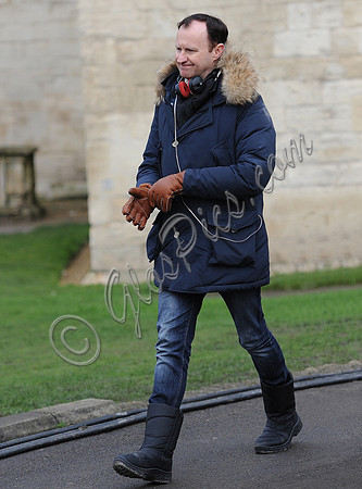 Mark Gatiss wearing fur collared blue Parka coat and leather gloves carrying polystyrene coffee cup