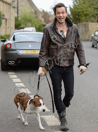 Jamie Hince wearing black skinny jeans, scruffy boots and brown bomber style leather jacket, with dog  "Archie" on lead.