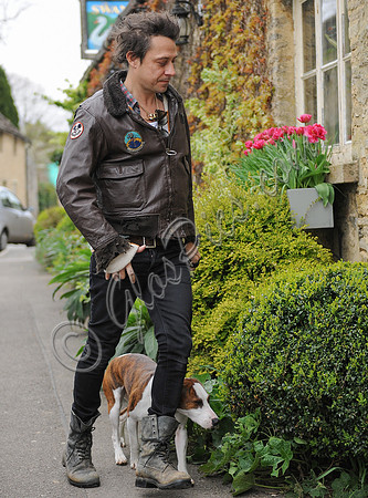 Jamie Hince wearing black skinny jeans, scruffy boots and brown bomber style leather jacket, with dog  "Archie" on lead.
