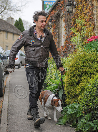 Jamie Hince wearing black skinny jeans, scruffy boots and brown bomber style leather jacket, with dog  "Archie" on lead.