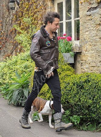 Jamie Hince wearing black skinny jeans, scruffy boots and brown bomber style leather jacket, with dog  "Archie" on lead.