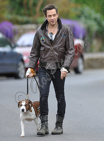 Jamie Hince wearing black skinny jeans, scruffy boots and brown bomber style leather jacket, with dog  "Archie" on lead.