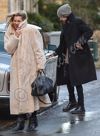 Kate Moss in calf length faux fur coat giggling with Jefferson Hack in background.