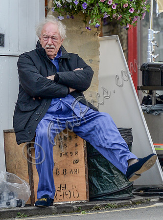 Sir Michael Gambon as Howard Mollison sat on tea chest wearing blue pyjamas and monogrammed slippers