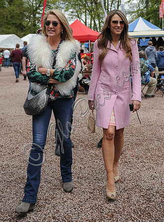 Georgia Daventry wearing jeans, brightly coloured blouse and fluffy gilet with Elizabeth Hurley in a pink coat both wearing sunglasses walking towards camera.