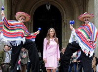 Elizabeth Hurley in pink coat flanked by  two mexicans on stilts wearing ponchos, sombreros and shaking their maracas