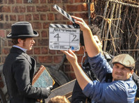 Ed Speleers side shot with a male wearing a flat cap holding up a clapperboard