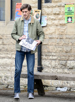 Mathew Baynton wearing khaki jacket , jeans and trainers holding a missing poster outside police station