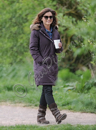 Jenna Coleman on 29th birthday, on set to film Doctor Who, walking and smiling at camera, wearing sunglasses and padded purple coat holding polystyrene cup
