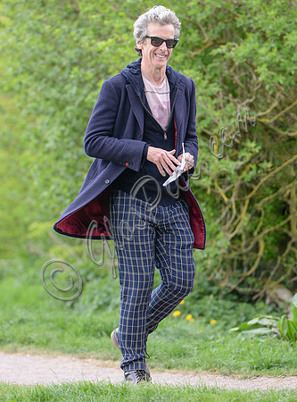 Peter Capaldi as Doctor Who wearing a long dark jacket, checked trousers and Ray Ban sunglasses