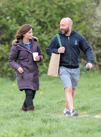Jenna Coleman walking along with crew member carrying her bag,  going on set to film Doctor Who, wearing sunglasses and padded purple coat holding polystyrene cup