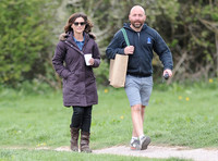 Jenna Coleman walking along with crew member carrying her bag,  going on set to film Doctor Who, wearing sunglasses and padded purple coat holding polystyrene cup