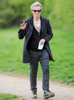 Full length shot of Peter Capaldi as Doctor Who wearing a long dark jacket, checked trousers and Ray Ban sunglasses waving to camera
