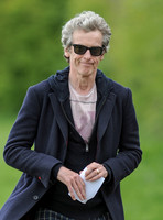 Close up of Peter Capaldi as Doctor Who wearing a long dark jacket, checked trousers and Ray Ban sunglasses