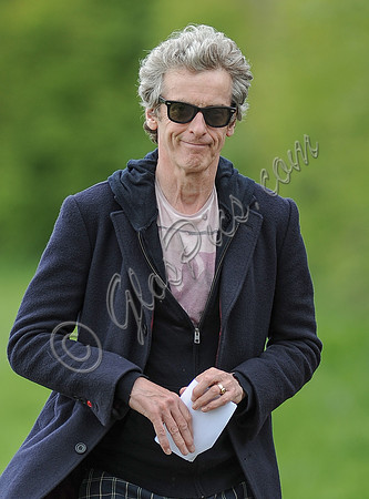Close up of Peter Capaldi as Doctor Who wearing a long dark jacket, checked trousers and Ray Ban sunglasses