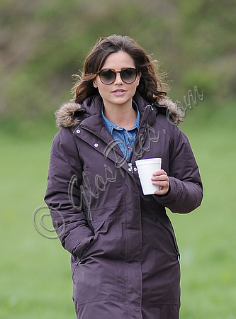 Waist up shot of Jenna Coleman on 29th birthday, on set to film Doctor Who, wearing sunglasses and padded purple coat holding polystyrene cup