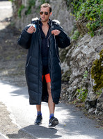 Matthew Lewis wears orange and black running gear covered by long black padded coat and glasses between takes