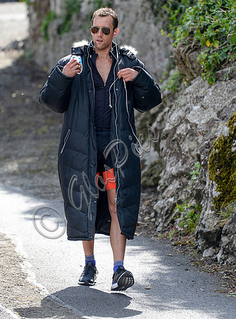 Matthew Lewis wears orange and black running gear covered by long black padded coat and glasses between takes