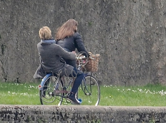 Emilia Clarke with Thea Sharrock riding pillion on bicycle, back view