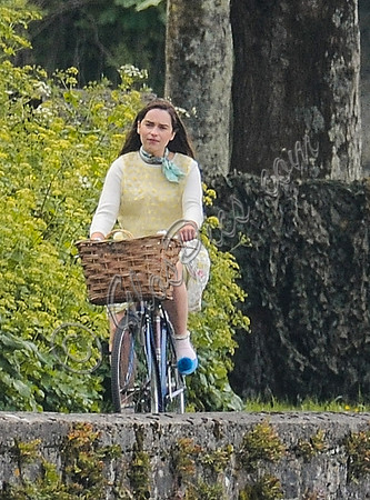 Emilia Clarke on bicycle with handlebar basket wearing lemon floral dress, lemon jumper and turquoise neckerchief