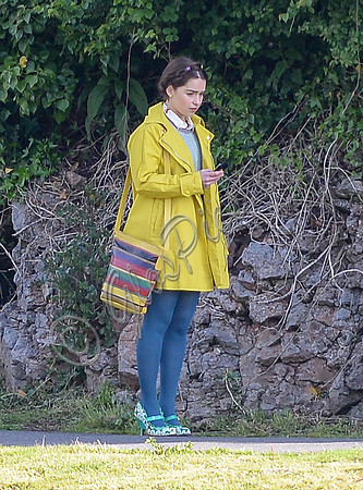 Emilia Clarke pictured on towpath wearing plaited hair, bright yellow coat, blue tights and green shoes.