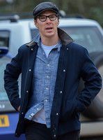 Benedict Cumberbatch wearing denim shirt, flat cap and glasses
