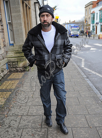 A bearded Nicolas Cage wearing plaid jacket and beanie hat, walking alone in Glastonbury, Somerset.