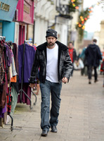 A bearded Nicolas Cage wearing plaid jacket and beanie hat, walking alone in Glastonbury, Somerset.