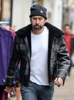 Close up of a bearded Nicolas Cage wearing plaid jacket and beanie hat, walking alone in Glastonbury, Somerset.