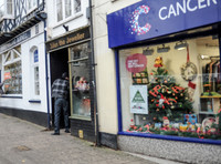 Nicolas Cage wearing plaid jacket and beanie hat emerging alone and backwards from "Julian the Jewellers", in Glastonbury, Somerset.