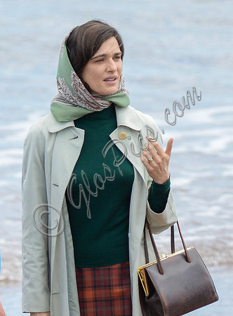 Close up of Rachel Weisz on beach carrying handbag, wearing 60's style pale green raincoat and headscarf