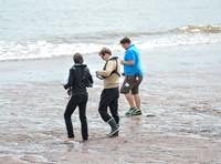 Colin Firth walking into the sea, wearing beige cardigan talking to director James Marsh