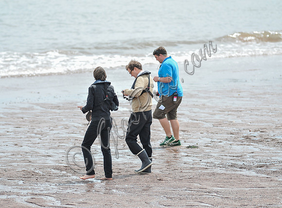 Colin Firth walking into the sea, wearing beige cardigan talking to director James Marsh
