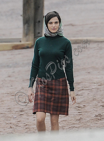 Rachel Weisz on beach wearing 60's style headscarf, green turtle neck sweater and red plaid 'A' line skirt and blue short wellington boots