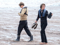 Colin Firth walking into the sea, wearing beige cardigan talking to director James Marsh