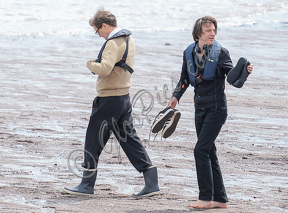 Colin Firth walking into the sea, wearing beige cardigan talking to director James Marsh