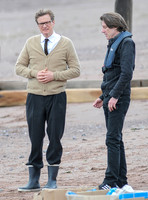 Colin Firth on Teignmouth beach, hands clenched loosely in front wearing beige cardigan talking to director James Marsh