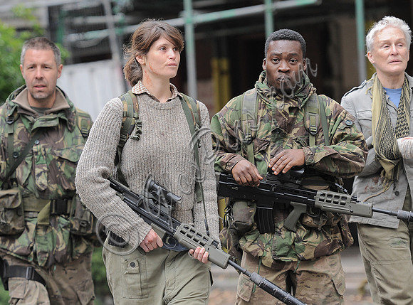 Glenn Close, Paddy Considine, Gemma Arterton and Fisayo Akinade all wearing fatigues and carrying weapons walking alongside each other waist up.