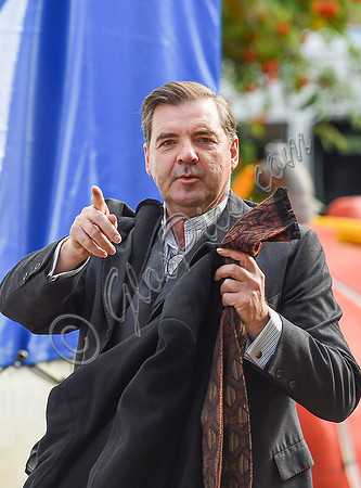 Brendan Coyle carrying a jacket and tie in left hand and gesticulating with his right.