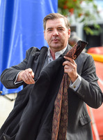 Brendan Coyle carrying a jacket and tie in left hand and gesticulating with his right.