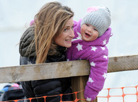 Dolly Maude carries  laughing Mia Tindall wearing pink and white all in one suit and woolly hat.