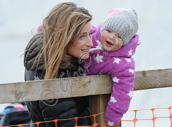 Dolly Maude carries  laughing Mia Tindall wearing pink and white all in one suit and woolly hat.