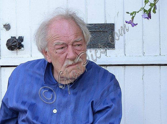 Sir Michael Gambon as Howard Mollison wearing blue pyjamas and monogrammed slippers